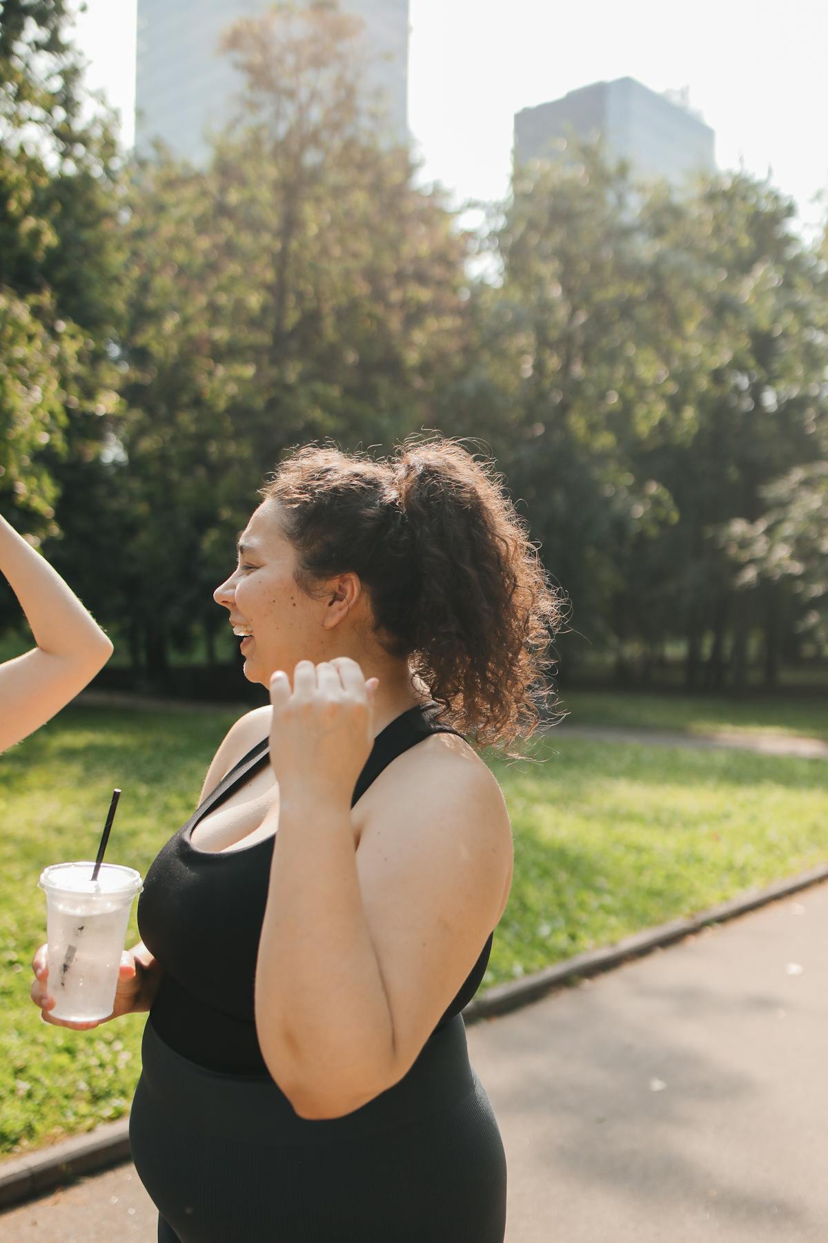 Woman laughing on a sunny walk with a healthy drink — staying active during weight loss